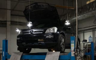 Used black car Mercedes Benz GL with an open hood raised on a four-post lift