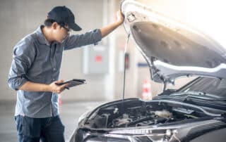 Asian auto mechanic holding digital tablet checking car engine