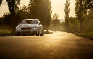 White car BMW 3 Series F30 is parked on empty countryside asphalt road at sunset