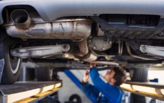 Exhaust of a car on the bridge at a European auto repair shop with a mechanic underneath